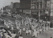 c 1964,  Approaching the corner of King and Stone streets, the town's main business corner, a parade is viewed by the town's citizens.